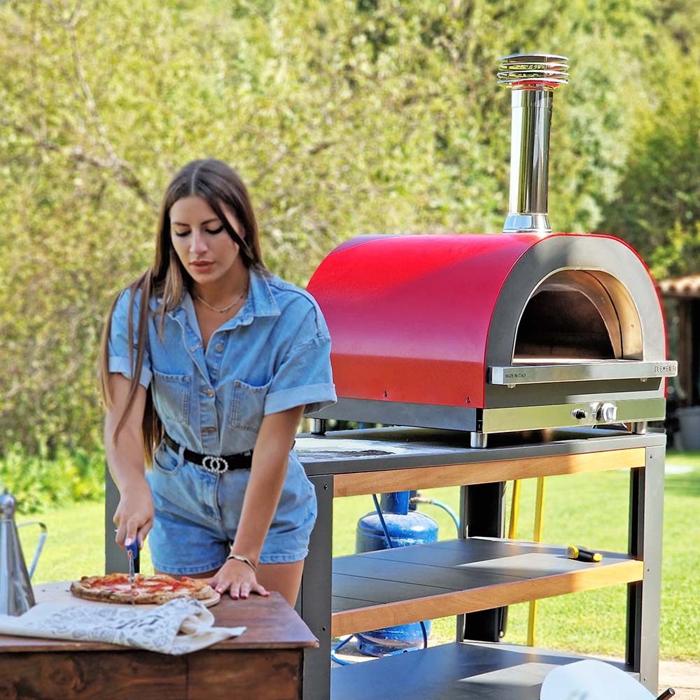 woman cutting pizza after cooking in clementi pizza oven