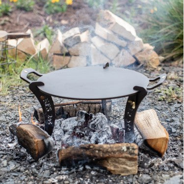 12‑inch black iron chapa griddle plate with detachable legs over campfire