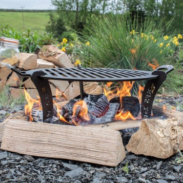 5‑inch black iron barbecue chapa with detachable legs over campfire