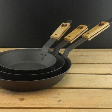 Set of three Netherton Foundry spun iron frying pans with oak handles on a wooden surface