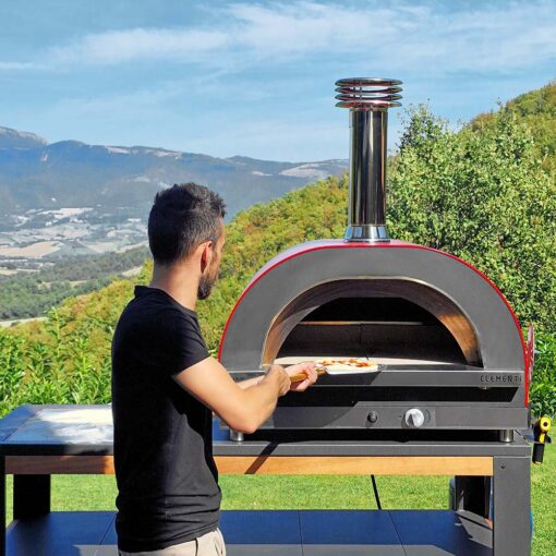 man placing pizza in clementi pizza oven outdoors