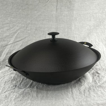 Compact spun iron wok with double handles on stone surface