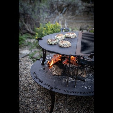 Elevated griddle plate and fire table on grass with fire burning