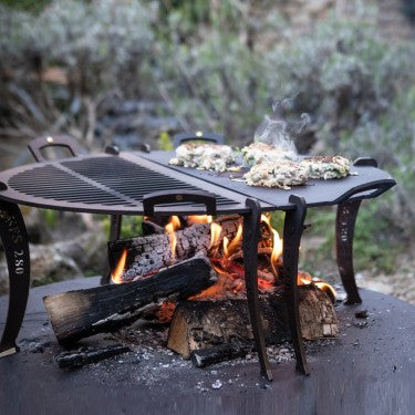 15‑inch black iron barbecue griddle with detachable legs over campfire