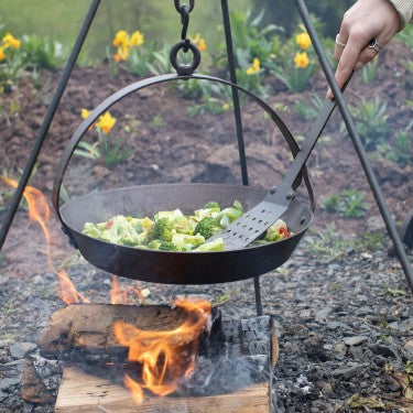 Spun iron Crochta pan suspended over open flame with food inside