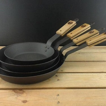 Oak-lidded spun iron saucepan and frying pan displayed together, ready for off‑grid cooking