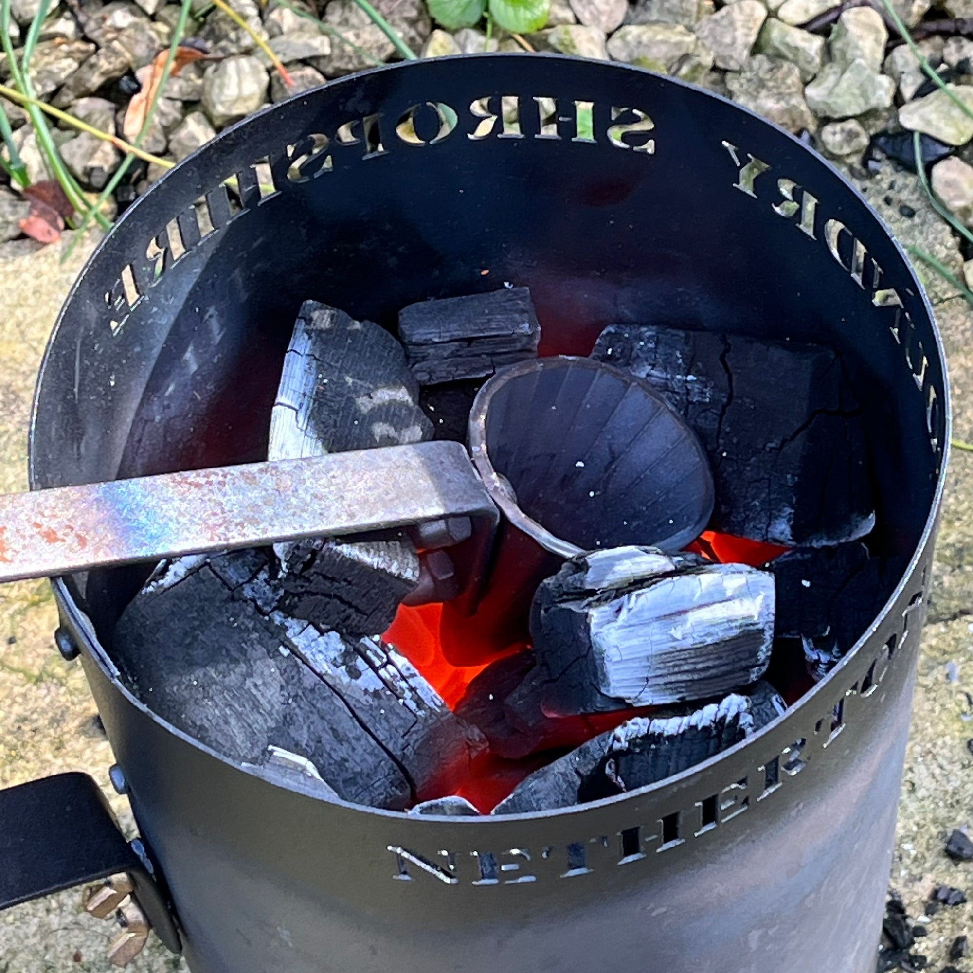 Charcoal chimney starter with charcoal and a tool on a stone surface