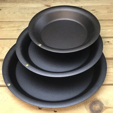 Three spun iron pie dishes stacked in rustic kitchen settin