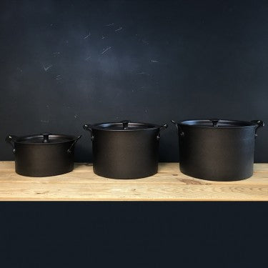 Set of three Netherton Foundry spun iron stockpots with lids on a wooden surface